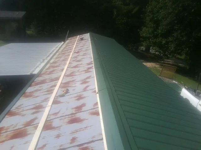 Old rusted panels beside newly installed green metal roofing — Wind Damage Roof Repair by Roofing Brothers in Logan
